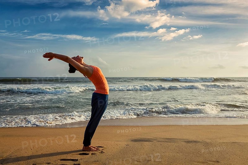 Young woman doing yoga Sun salutation Surya Namaskar pose Hasta Uttanasana on tropical beach on sunset
