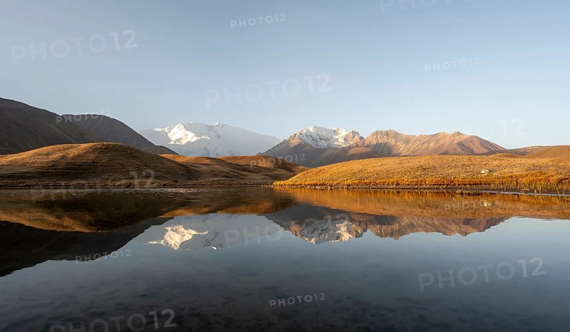 White glaciated and snowy mountain peak Pik Lenin at sunrise, mountains reflected in a lake between golden hills, Trans Alay Mountains, Pamir Mountains, Osh Province, Kyrgyzstan, Asia