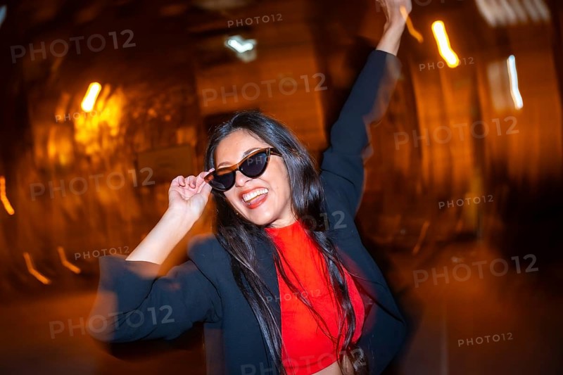 Night photo with flash and motion of a cool woman with sunglasses celebrating dancing in the city at night
