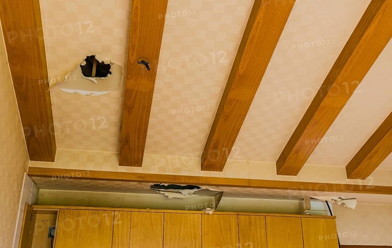 Holes and torn wallpaper in ceiling above kitchen cabinets in abandoned house