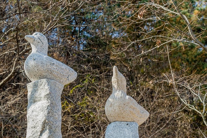 Closeup of stone carved ducks on vertical plinths in wilderness park with trees in fall colors