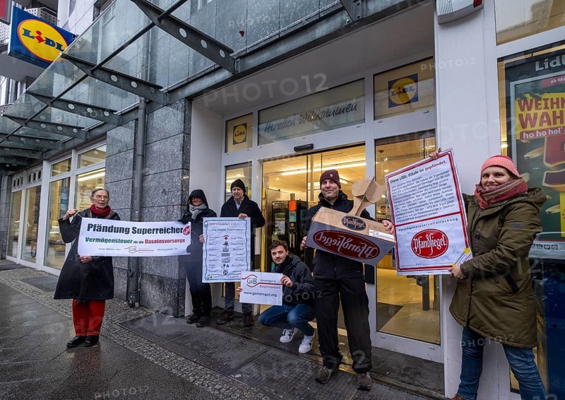 Germany, Berlin, 21.12.2023, action by Gemeingut in BuergerInnenhand (GiB), actions in front of branches of LIDL, Aldi and BMW, here a Lidl branch in Luisenstrasse / Berlin-Mitte, activists press a large deposit seal on a door of the LIDL branch, Carl Wassmuth, spokesman for Gemeingut: Super-rich like LIDL owner Dieter Schwarz only pay tiny tax rates, Europe