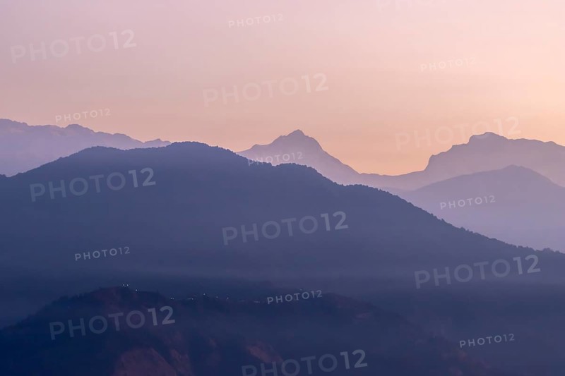 Silhouette of the eight-thousander Manaslu and some other Himalayan peaks, including Ngadi Chuli, seen at daybreak from Sarangkot, the popular viewpoint above Pokhara, from the distance of nearly 70 km. The clear, January sky illuminates orange and violet, contrasting the contours of the dark mountains. Kaski District, Gandaki Province, Nepal, Asia