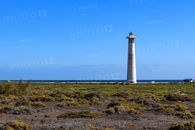 View of lighthouse Faro de Morro Jable on east coast of peninsula Jandia, in the foreground green plants ground cover vegetation on ground of volcanic origin, in the background blue sea east atlantic Atlantic, above bright blue sky, on the horizon light clouds, Morro Jable, peninsula Jandia, Fuerteventura, Canary Islands, Spain, Europe