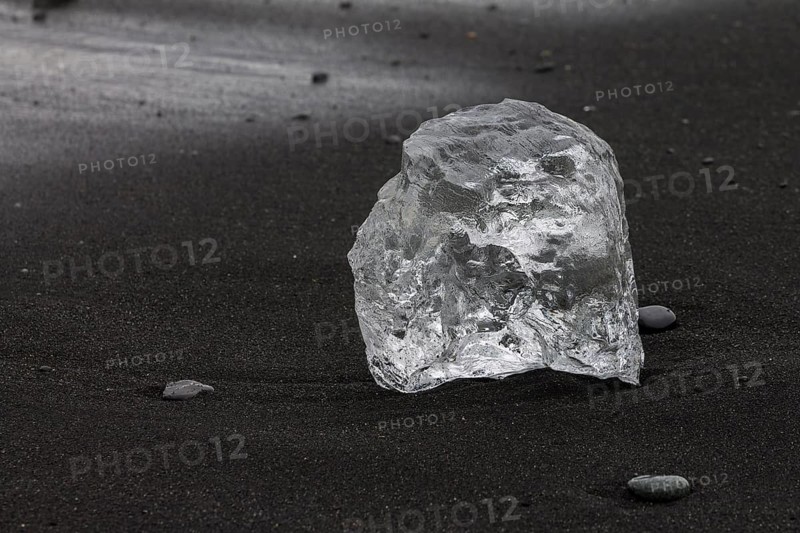 A piece of glacial ice, melting on the black sand beach near Joekulsarlon glacial lake on the Atlantic Ocean coast, known as diamond beach. Photographed in summer. Sveitarfelagio Hornafjoerour, Suourland, Southern Region, Iceland, Europe