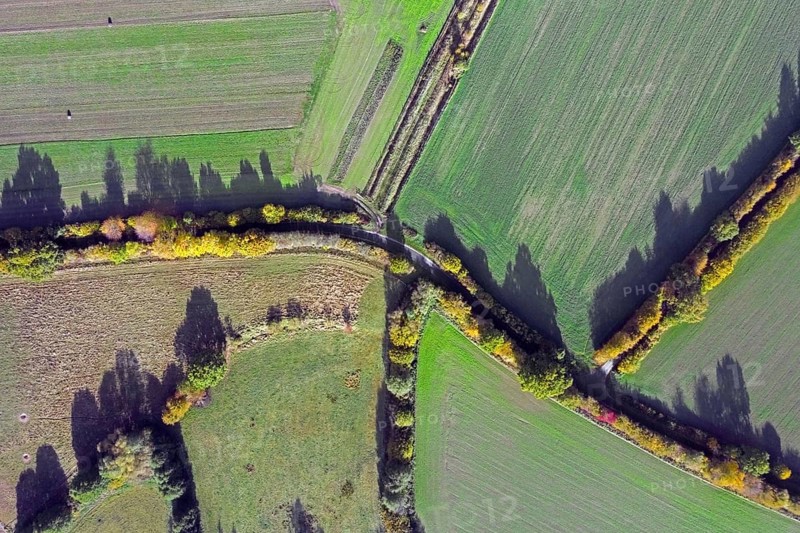 Aerial view over rural roads and bocage landscape with fields, meadows and pastures, patchwork of plots surrounded by hedges and hedgerows in autumn