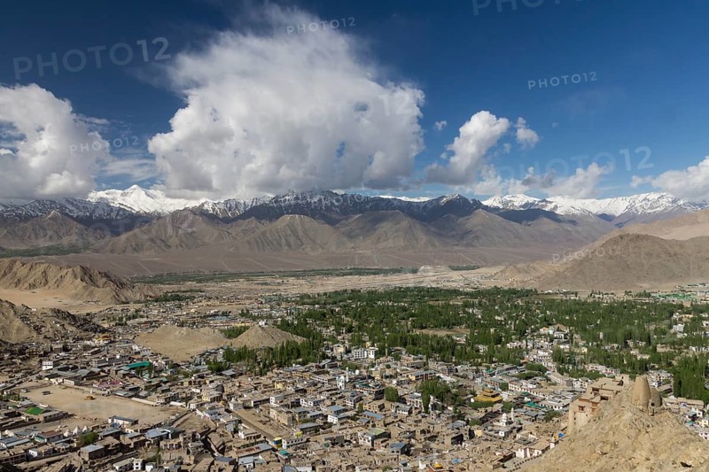 Leh, the capital town of Ladakh and main settlement in the region, with the Indus Valley below and the Stok Range of the Zanskar Mountain, Himalayas, in the distance. Seen from Namgyal Tsemo, The Victory Hill, with a big, white cloud on the otherwise fairly clear, blue sky. Photographed in late May, the springtime. District Leh, Union Territory of Ladakh, India, Asia