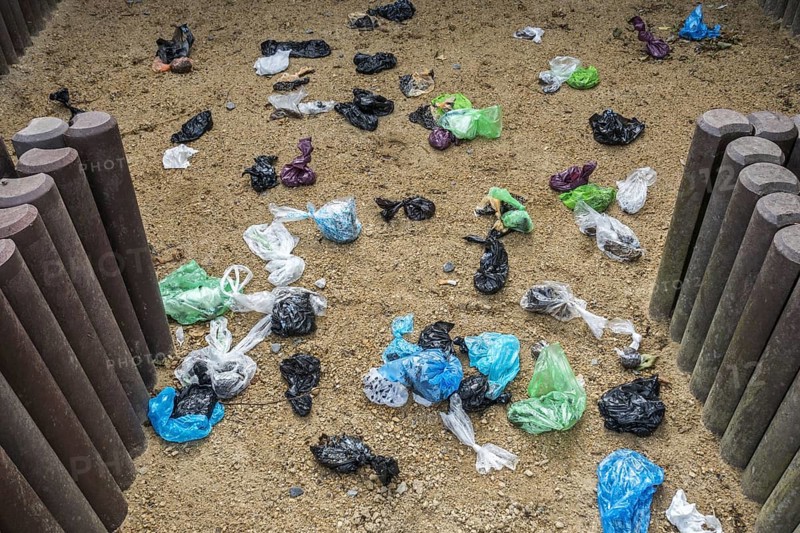 Fenced sandy public dog toilet area in city park filled with colourful discarded plastic dog poop bags