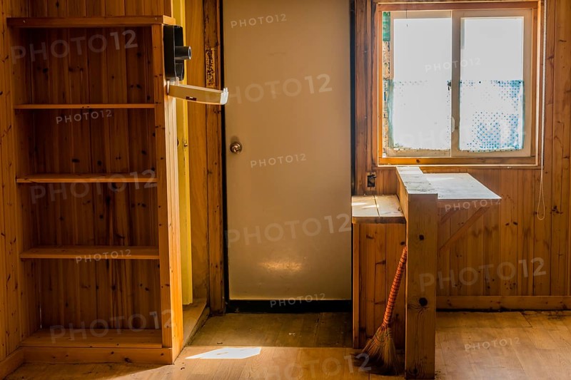 Sun shining through window into abandoned rustic cabin with built-in bookcase and kitchen bar