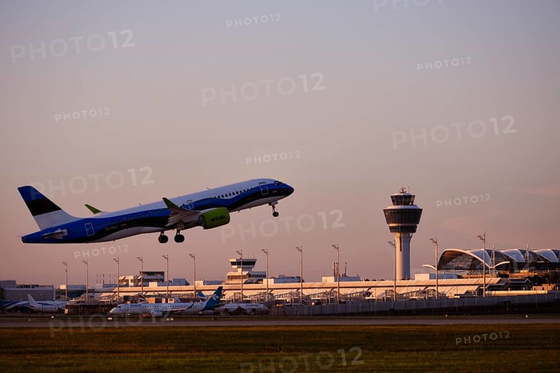 AirBaltic Airbus A220 taking off on Runway South with Terminal 1 and Tower in the sunset, Munich Airport, Upper Bavaria, Bavaria, Germany, Europe