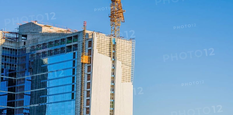 Yellow crane elevator attached to side of building that is under construction against a clear blue sky