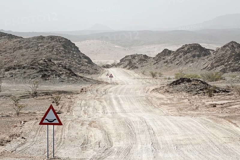 A warning sign stands in front of a sandy desert road, Safari, GravelRoad, unpaved roads, gravel roads, gravel surface, Namibia, Africa