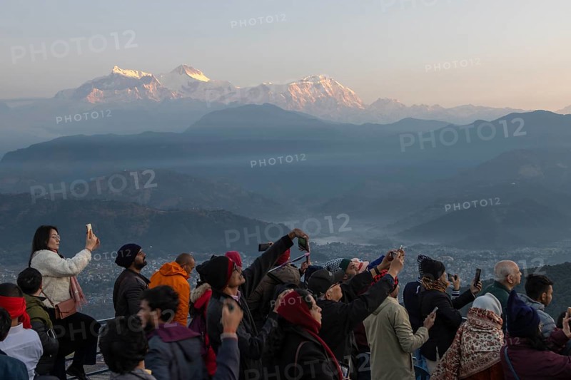 Asian-looking tourists watching and photographing sunrise as well as shooting selfies on the second day of the 2024 year from Sarangkot, with mountains of the Annapurna Massif in the background. Pokhara, Kaski District, Gandaki Province, Nepal, Asia
