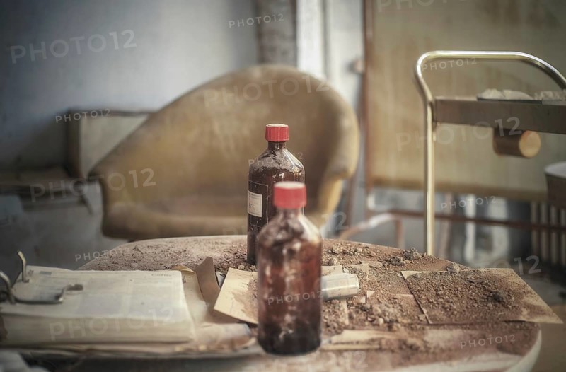 An old cloudy bottle on a dirty table next to a rusty hospital trolley, urologist's villa Dr Anna L., Lost Place, Bad Wildungen, Hesse, Germany, Europe