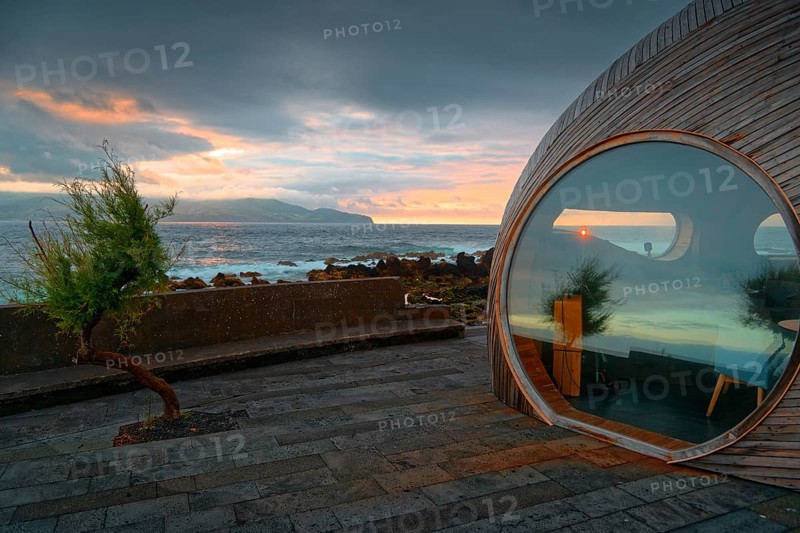 Round window of the wooden extension of the famous Calla Bar and view of the coast at sunset, Madalena, Pico, Azores, Portugal, Europe