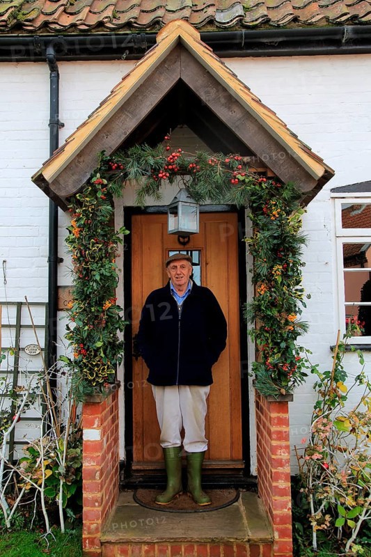 Elderly man standing in his porch having decorated it for Christmas, Suffolk, England, UK