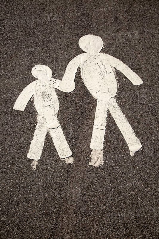 Child and parent figures holding hands on tarmac pavement, Mumbles, South Wales, UK