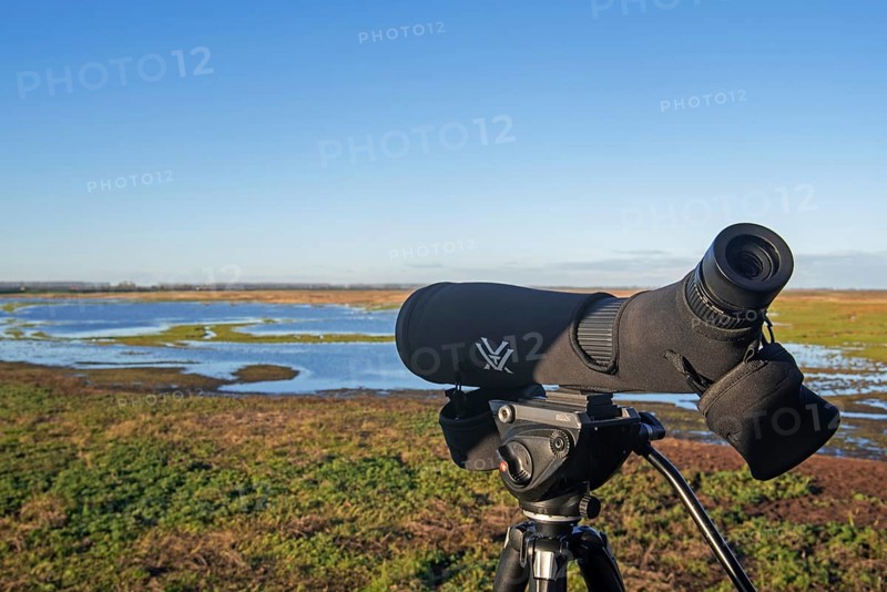 Birdwatcher's telescope and view over salt marsh of the Western Scheldt estuary at nature reserve Verdronken Land van Saeftinghe, Netherlands