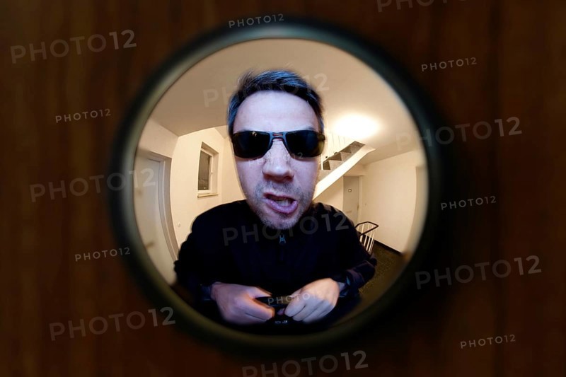 View through door viewer into a staircase, peephole, spyhole, with a man in front of the door, looking very angry, maybe landlord or bailiff