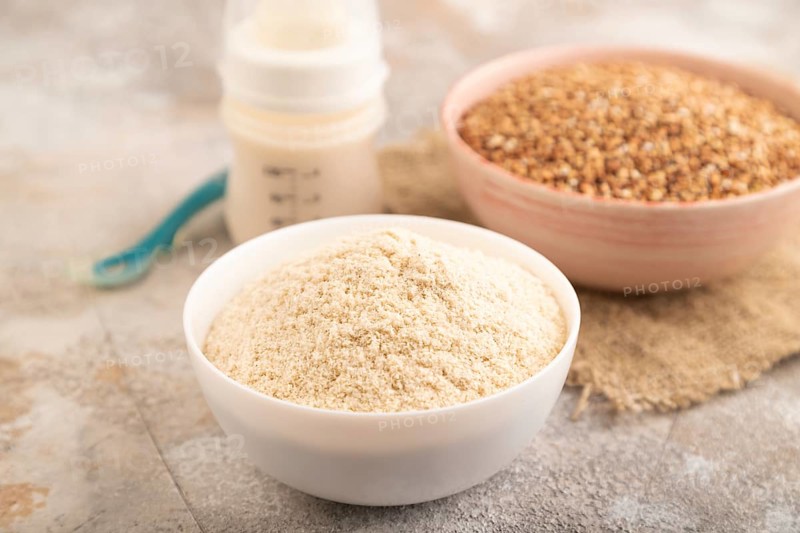 Powdered milk and buckwheat baby food mix, infant formula, pacifier, bottle, spoon on brown concrete background and linen textile. Side view, close up, selective focus, artificial feeding concept