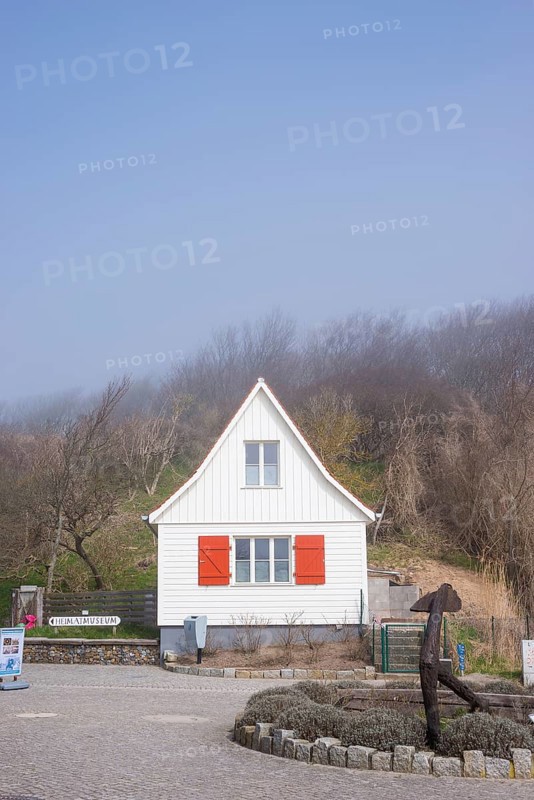Old, white wooden house with red shutters stands in the fog, old anchor, sea fog, wind fugitive, village Kloster, island Hiddensee, Baltic Sea, Germany, Europe