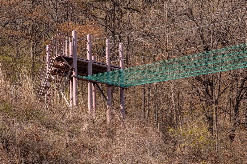Fire brigade training tower and attached safety net used to practice balance located in mountainside with blue sky with puffy white clouds in background