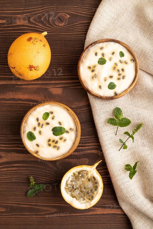 Yoghurt with granadilla and mint in wooden bowl on brown wooden background and linen textile. top view, flat lay, close up