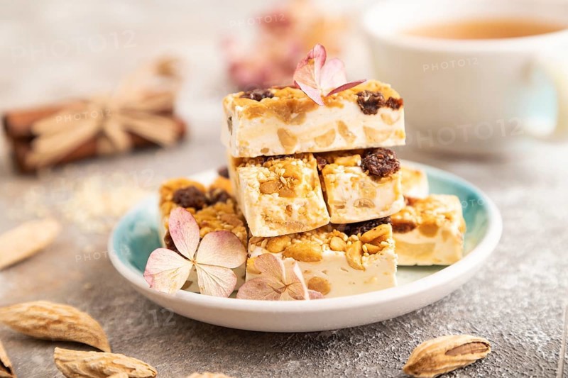 Traditional candy nougat with nuts and sesame with cup of green tea on brown concrete background. side view, close up, selective focus