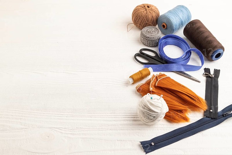 Sewing accessories: scissors, thread, thimbles, braid on white wooden background. Side view, copy space