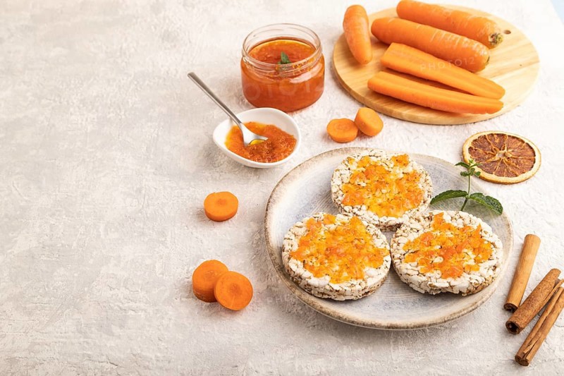 Carrot jam with puffed rice cakes on gray concrete background. Side view, copy space