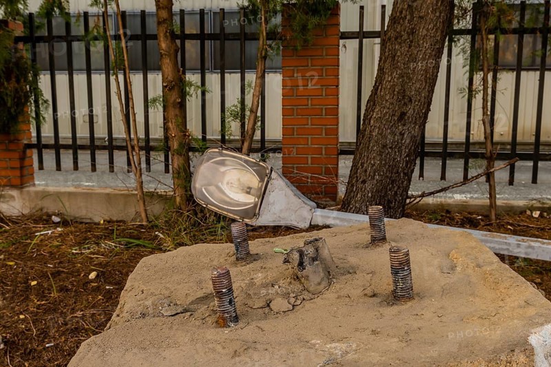 Old dismantled streetlight removed from lamppost and laying on ground behind concrete streetlamp base