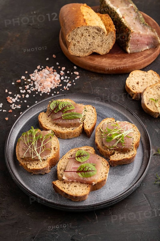 Bread sandwiches with jerky salted meat, sorrel and cilantro microgreen on black concrete background. side view, close up