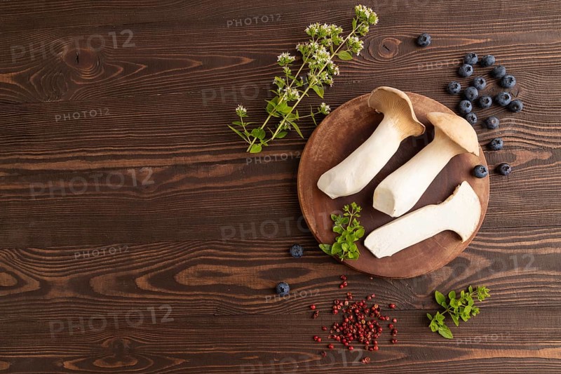 King Oyster mushrooms or Eringi (Pleurotus eryngii) on brown wooden background with blueberry, herbs and spices. Top view, flat lay, copy space