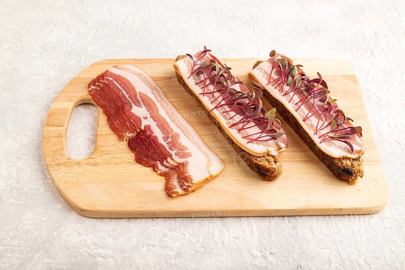 Bread sandwiches with jerky salted meat and lard with beet microgreen on gray concrete background. side view, close up