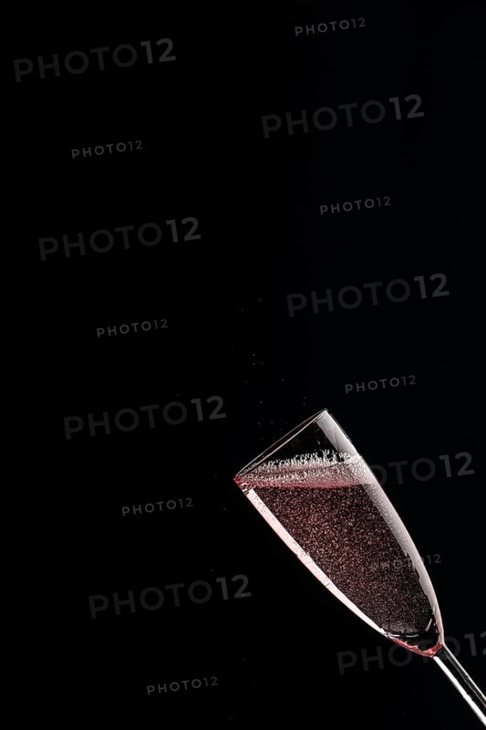 A champagne glass filled with rose sparkling wine against a black background