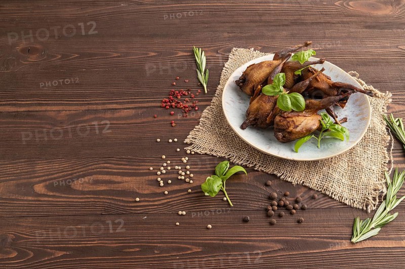 Smoked quails with herbs and spices on a ceramic plate with linen textile on a brown wooden background. Side view, copy space