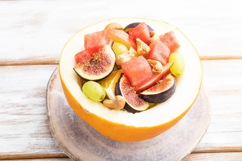 Vegetarian fruit salad of watermelon, grapes, figs, pear, orange, cashew on white wooden background. Side view, close up