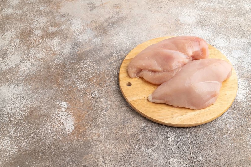 Raw chicken breast on a wooden cutting board on a brown concrete background. Side view, copy space