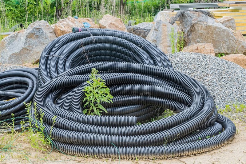 Black flexible pipe coiled and laying on ground at construction site