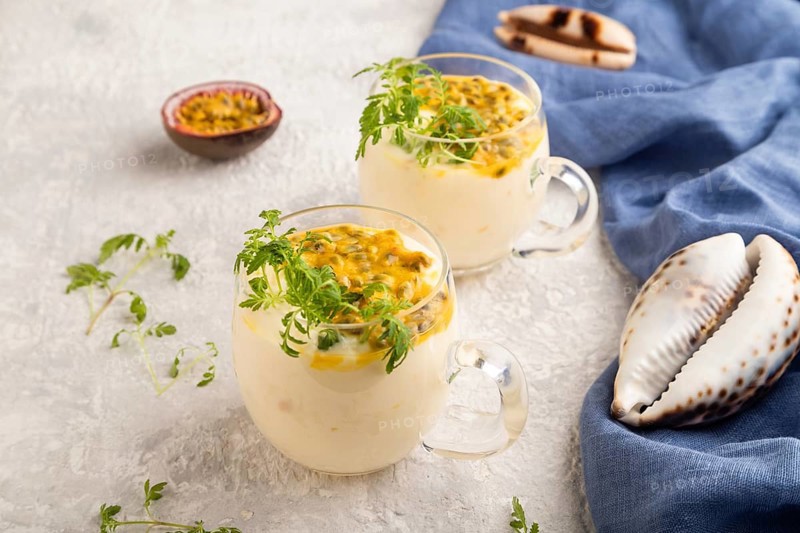 Yogurt with passionfruit and marigold microgreen in glass on gray concrete background with blue linen textile. Side view, close up