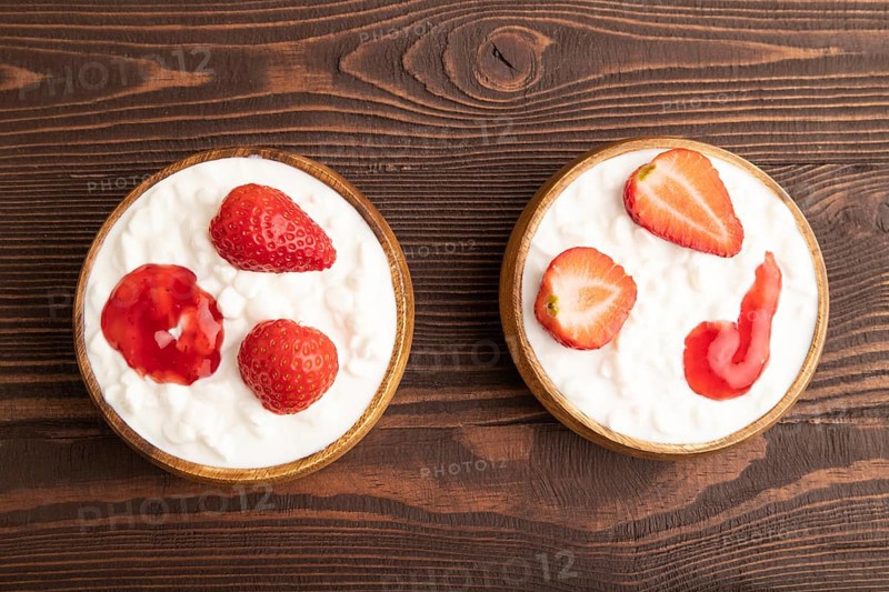 Grained cottage cheese with strawberry jam on brown wooden background. top view, flat lay, copy space