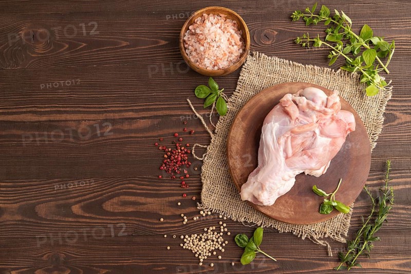 Raw turkey wing with herbs and spices on a wooden cutting board on a brown wooden background and linen textile. Top view, flat lay, copy space