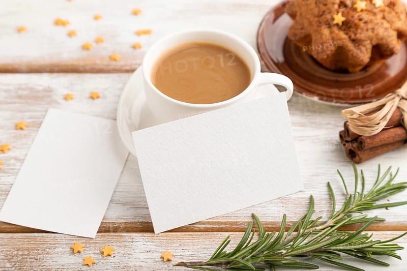White paper business card mockup with cup of coffee and cake on white wooden background. Blank, side view, still life