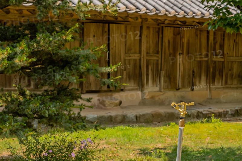 Copper water sprinkler in grassy lawn in front of wooden building located in public park displaying traditional Korean architecture