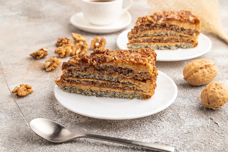 Walnut and hazelnut cake with caramel cream, cup of coffee on brown concrete background. side view