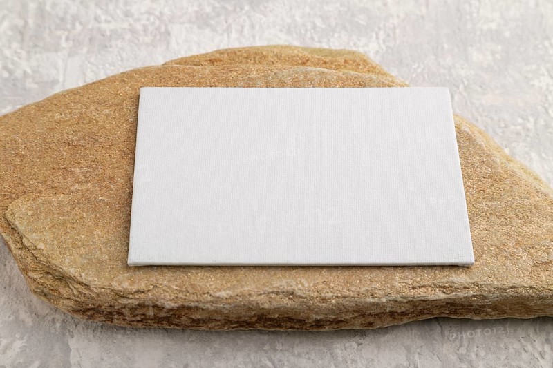 White paper business card, mockup with natural stone on gray concrete background. Blank, side view, still life, copy space, canvas