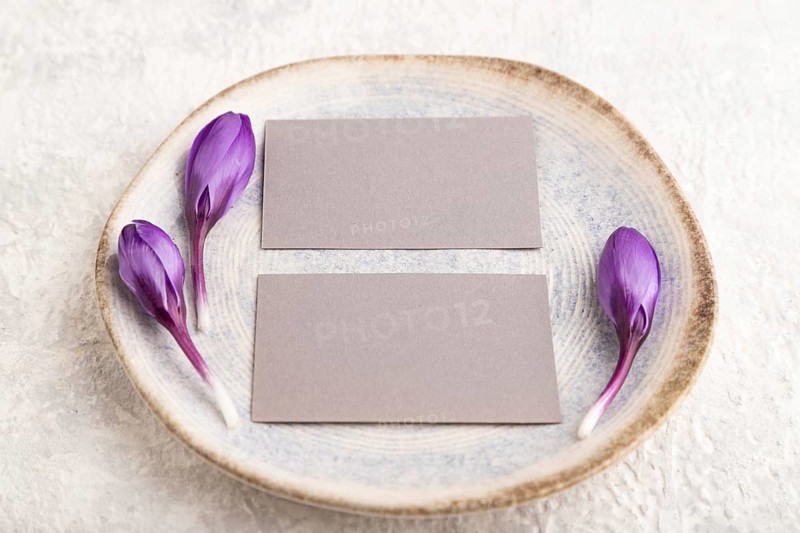 Gray paper invitation card, mockup with crocus flowers on ceramic plate and gray concrete background. Blank, flat lay, top view, still life, copy space, wedding invitation