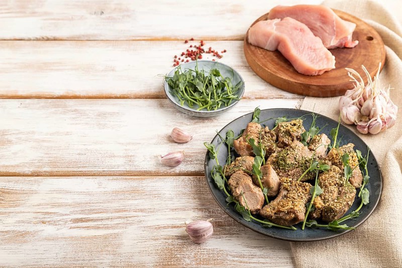 Stewed turkey fillet with garlic and sprouts of green peas on white wooden background and linen textile. Side view, copy space