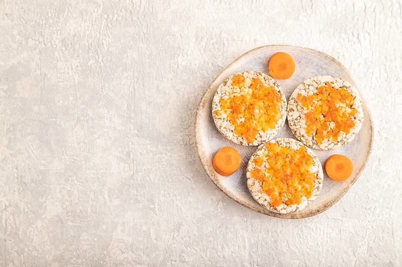 Carrot jam with puffed rice cakes on gray concrete background. Top view, flat lay, copy space