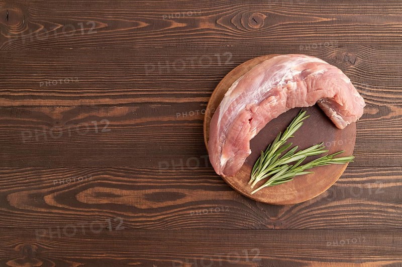 Raw pork with herbs and spices on a wooden cutting board on a brown wooden background. Top view, flat lay, copy space